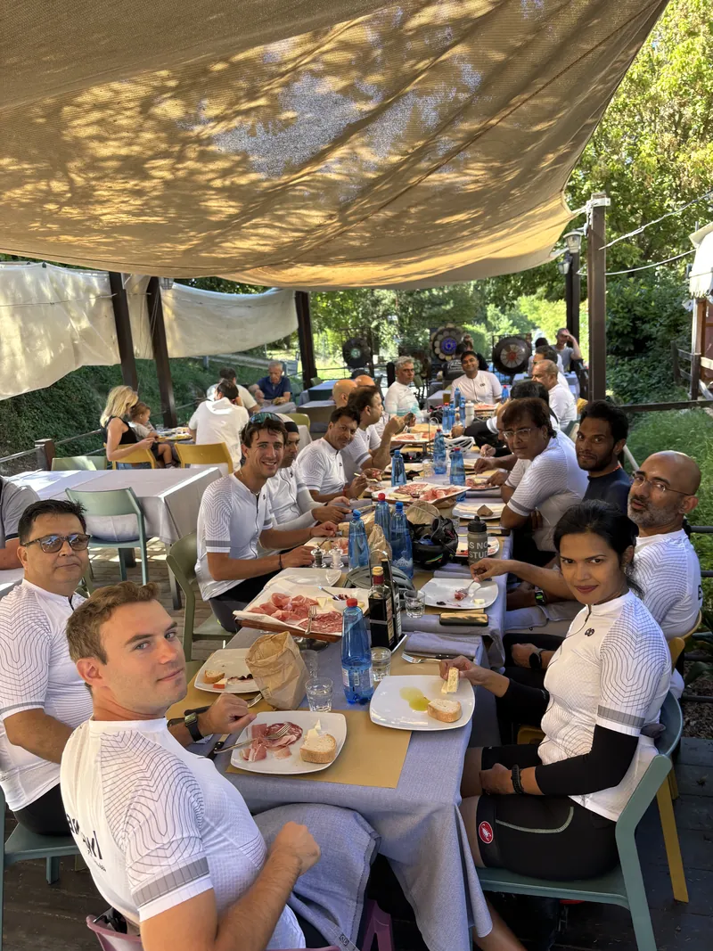 Riders in matching white jerseys at a long lunch table under a shade canopy