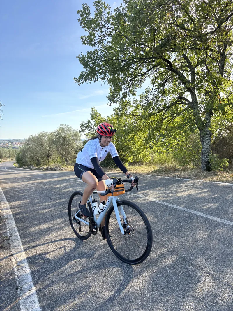 A rider in a white jersey riding towards the camera on a sunlit road