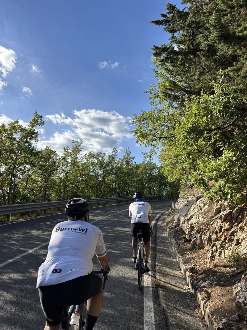 Two riders climbing a road beside a rock face, one in a Barnowl jersey