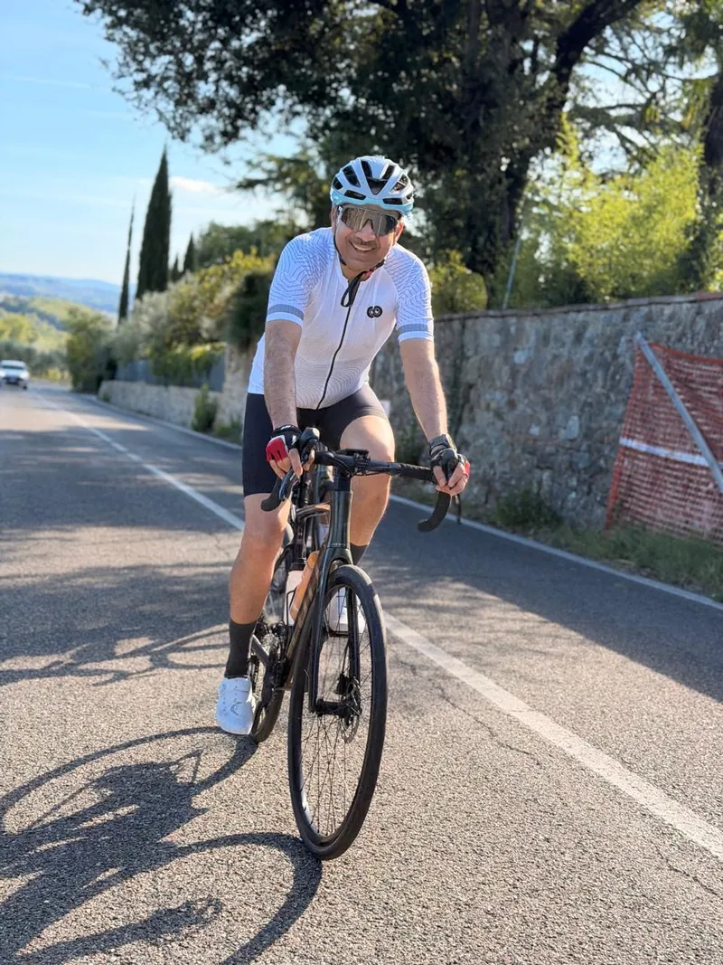 A rider in white riding past a stone wall, cypress trees behind
