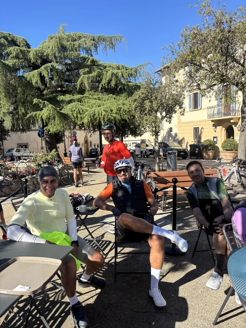 Riders at café tables in a town square, bikes leaning beside them