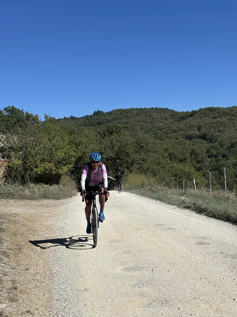 A rider on a white gravel road through wooded hills