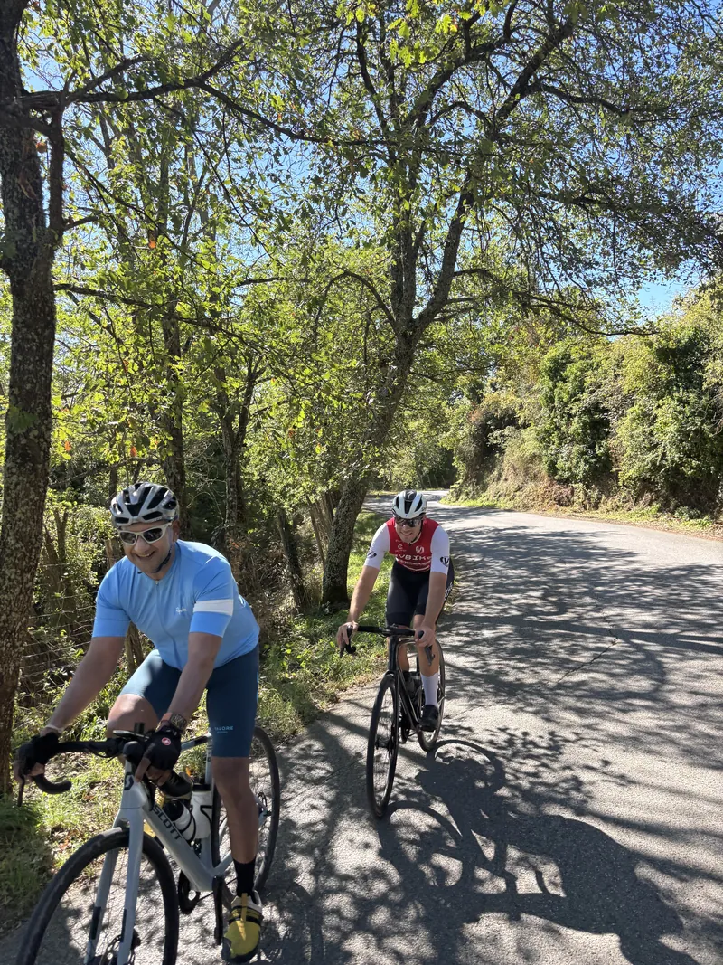 Two riders on a tree-lined road in dappled light