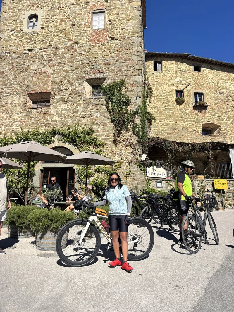 A rider with her bike outside a café in a stone tower, another rider behind