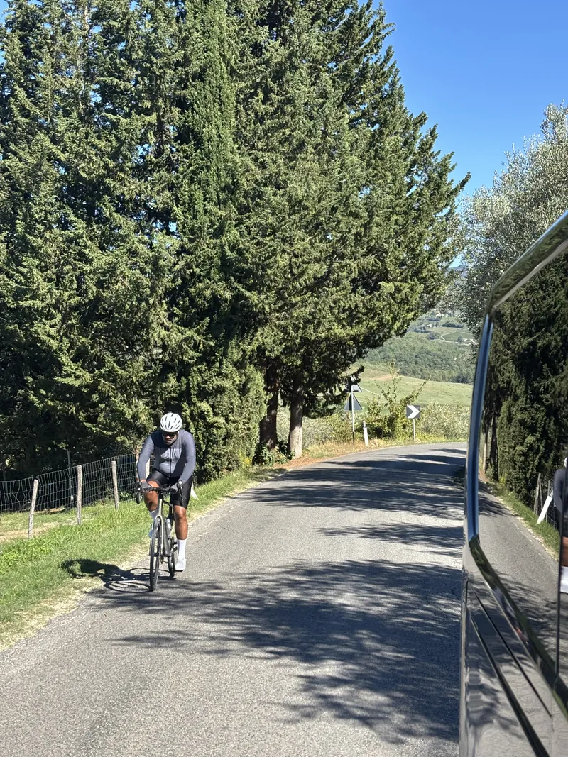A rider climbing a narrow road lined with tall trees