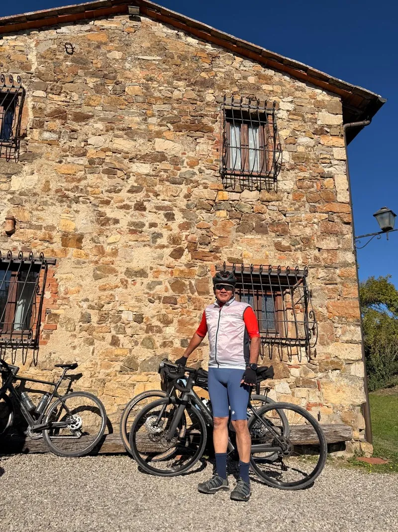 A rider with his bike beside a stone building with barred windows