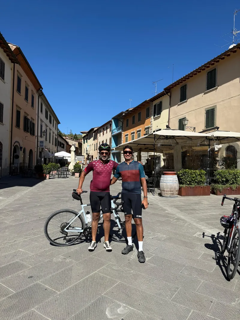 Two riders with a bike in a town square lined with old buildings