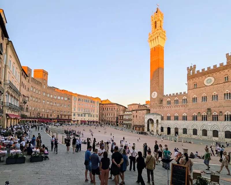 Piazza del Campo in Siena at dusk, the Torre del Mangia lit by the low sun