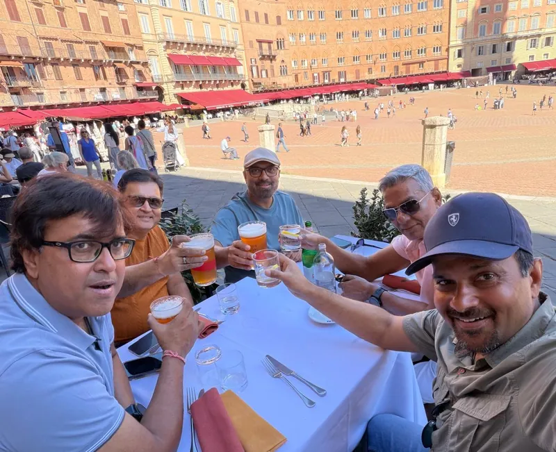Riders raising glasses at a table above Piazza del Campo
