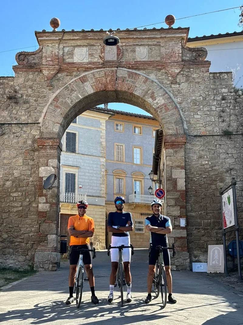 Three riders with their bikes under an old brick archway