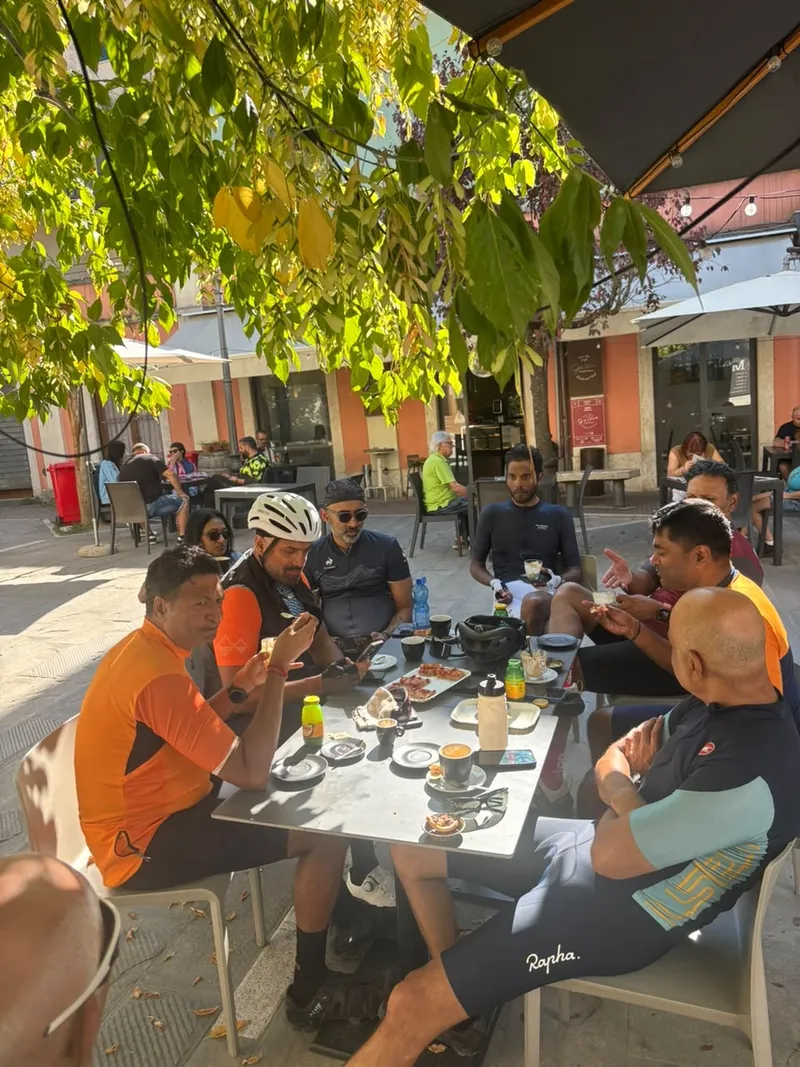 Riders at a café table in a town square, under a tree