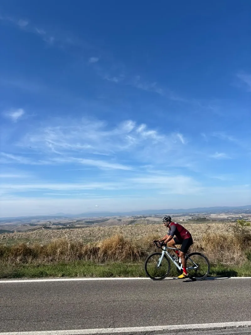 A rider on a road with wide, pale hills and a big sky behind