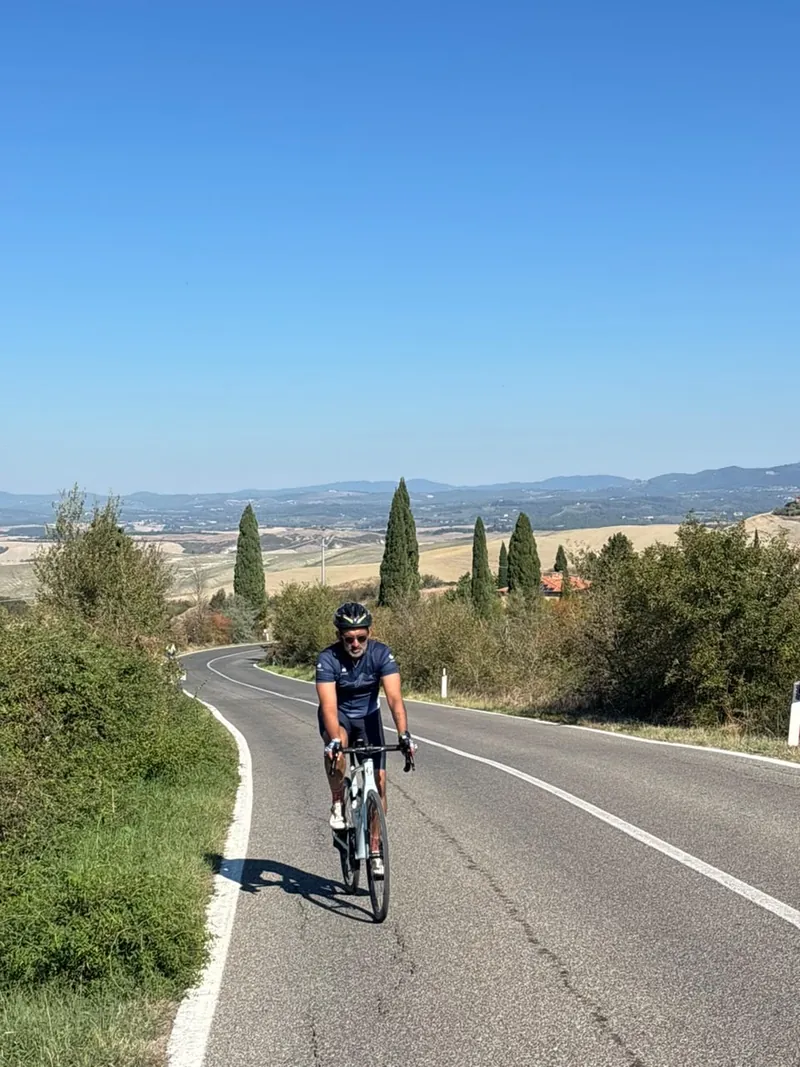 A rider on a curving road, cypress trees and distant hills behind