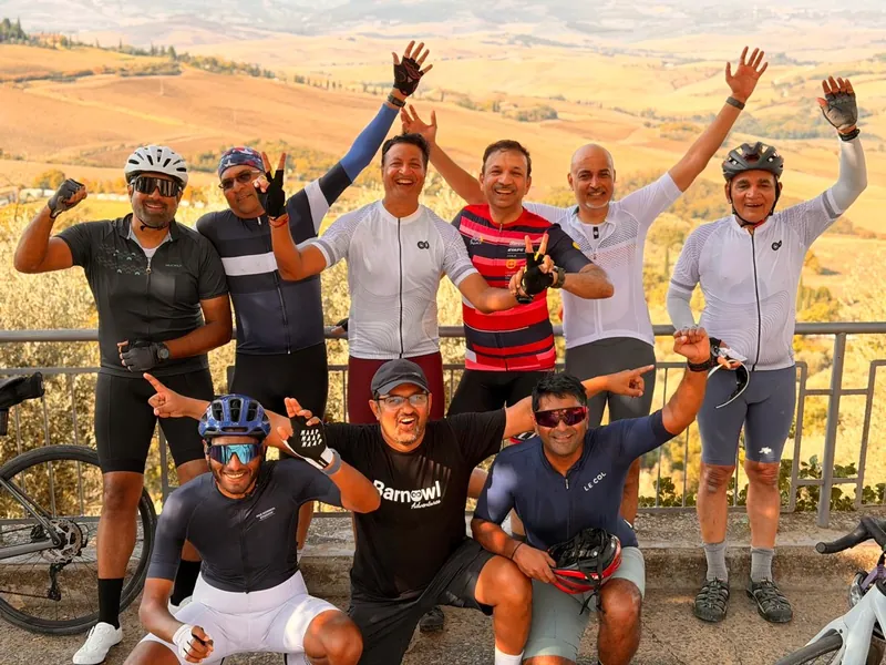Riders cheering with arms raised, the rolling hills of the Val d'Orcia behind
