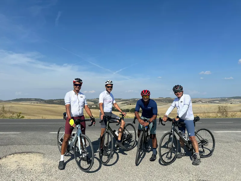 Four riders with their bikes on a roadside above open farmland