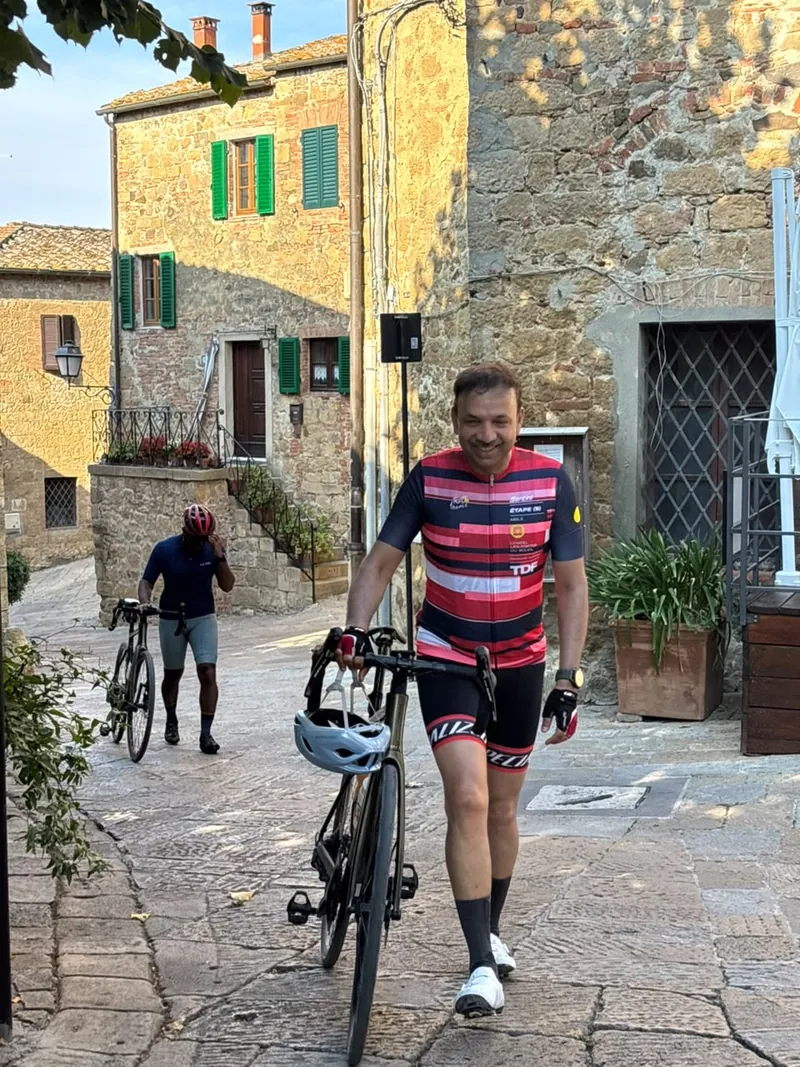 A rider walking his bike across a stone-paved square in a hill village
