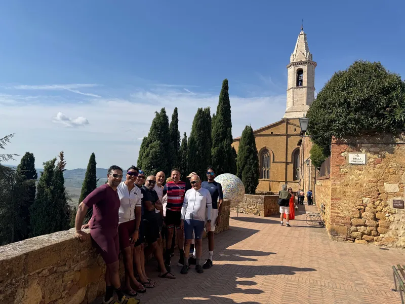 The group by a wall in a hill town, a church bell tower and cypresses behind