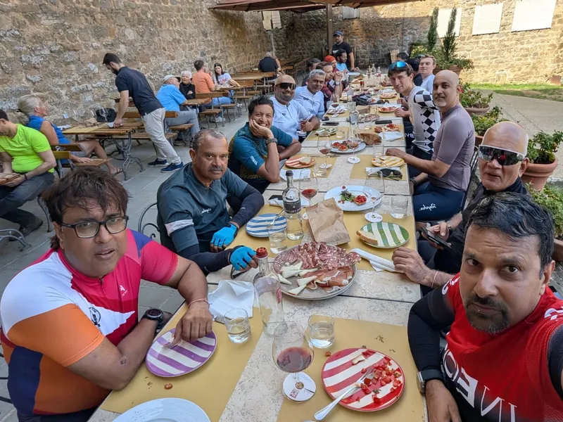 Riders at a long lunch table set outdoors beside a stone wall