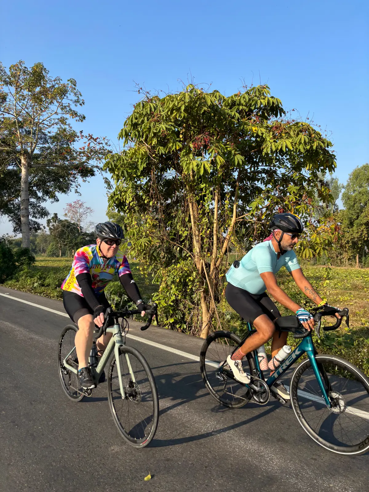 Two riders side by side on a tree-shaded road in northern Thailand