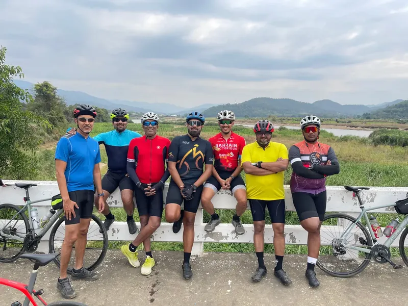 Seven riders and their bikes along a low wall, with hills and a river valley behind