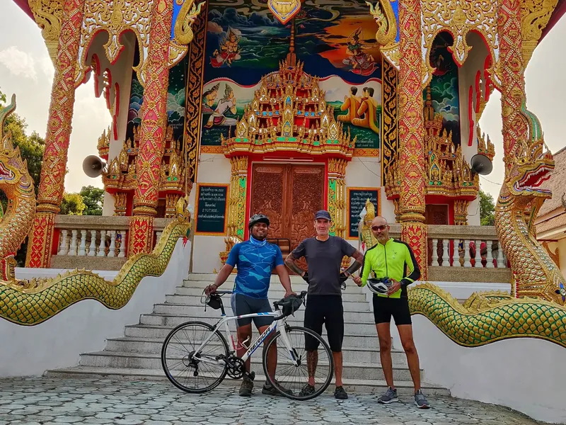 Riders with their bikes at an ornate temple entrance flanked by naga balustrades