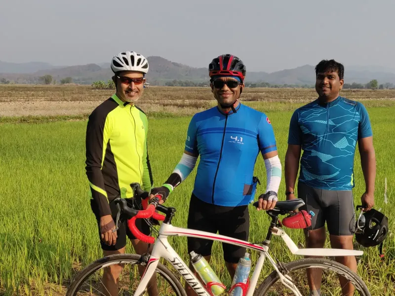 Three riders standing with their bikes in front of green rice fields