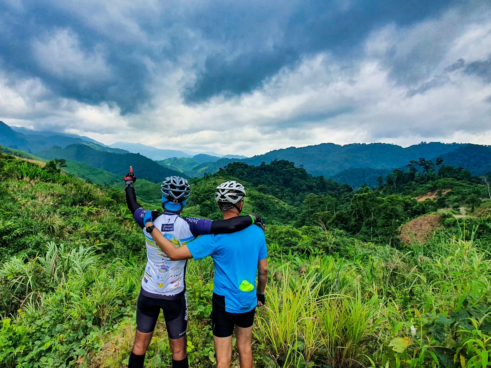 Two riders looking out over the forested Truong Son mountains under heavy cloud